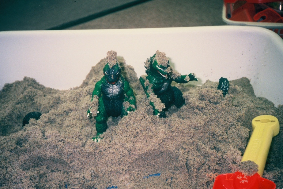 A toy godzilla in the sand Description automatically generated